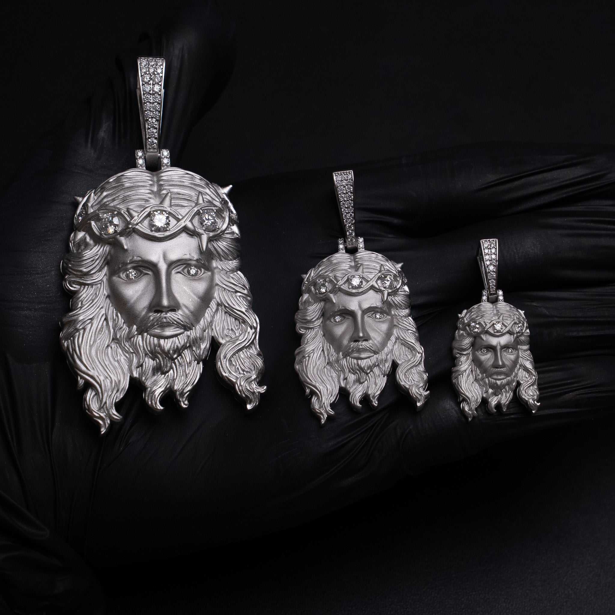 Three sizes of 925 sterling silver Jesus Piece Pendants with detailed facial features and crown of thorns, displayed on black gloved hand.