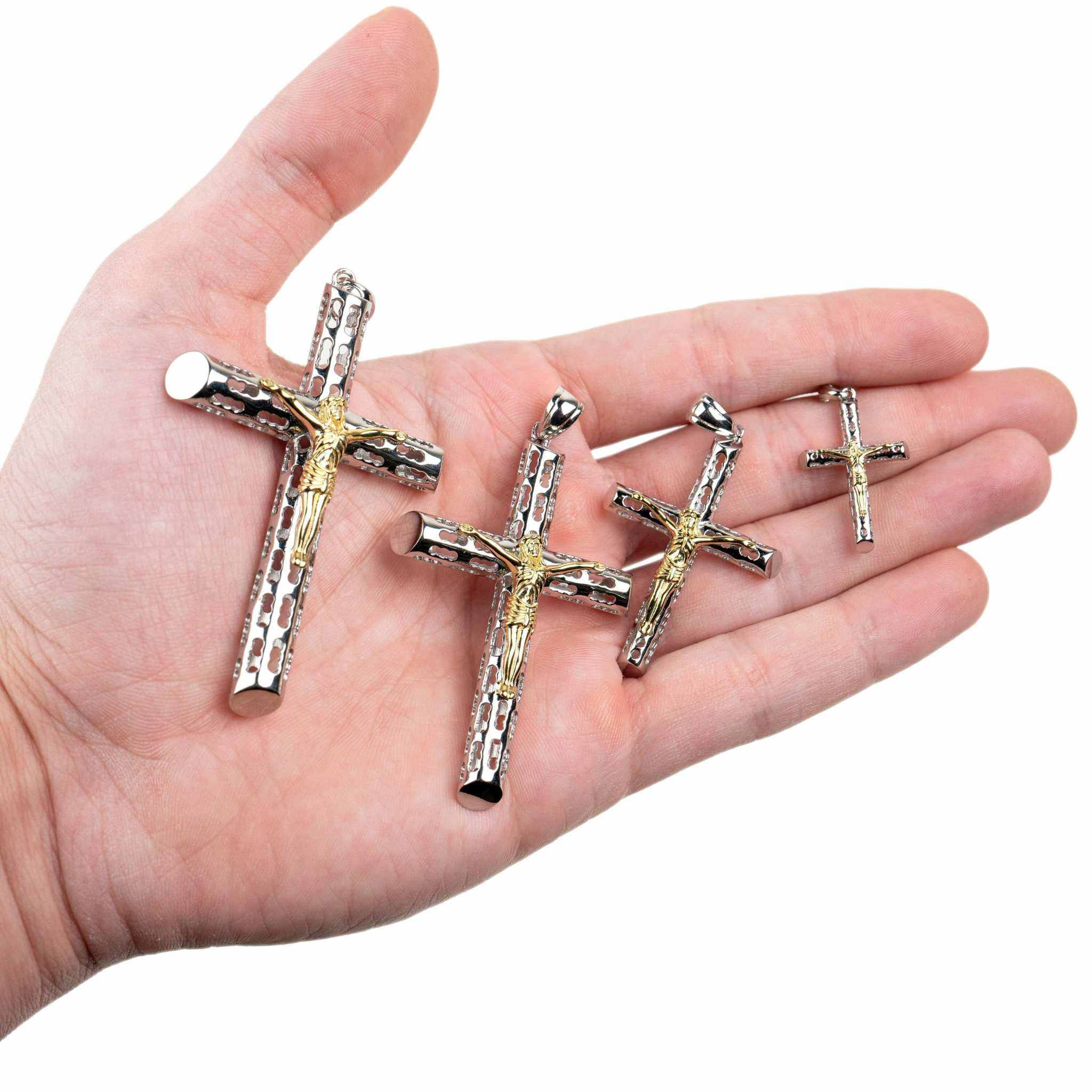 Two tone Jesus crucifix cross pendants in various sizes on a hand.