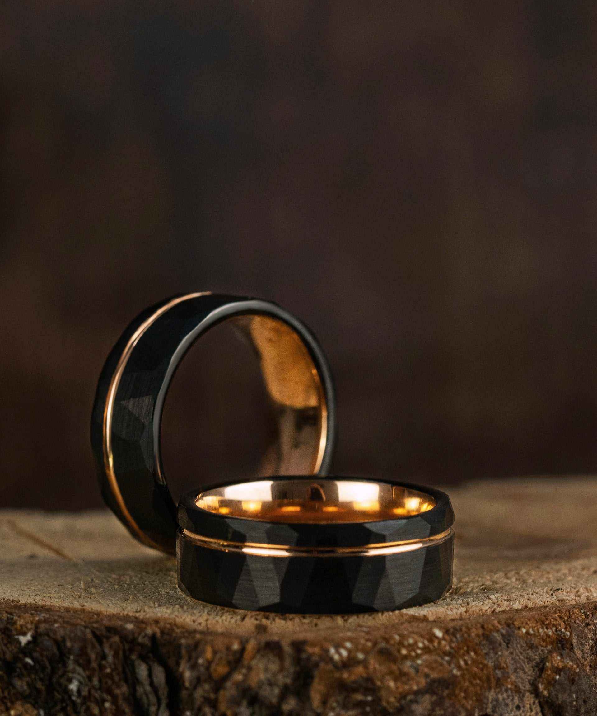 Black tungsten rings with gold interior on rustic surface.