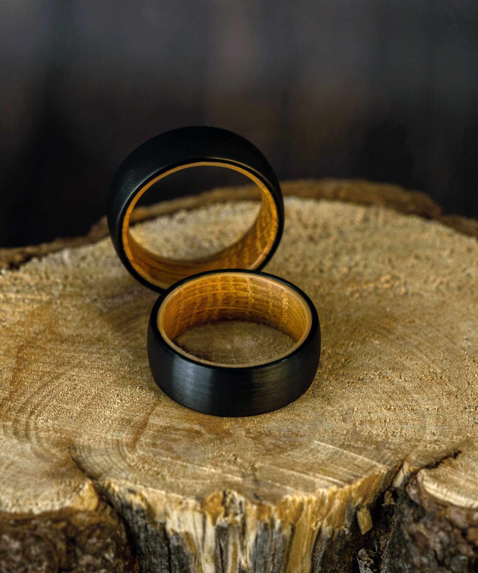 Plain Whiskey Barrel Ring with black satin tungsten finish and olive wood inner band on a wooden surface.