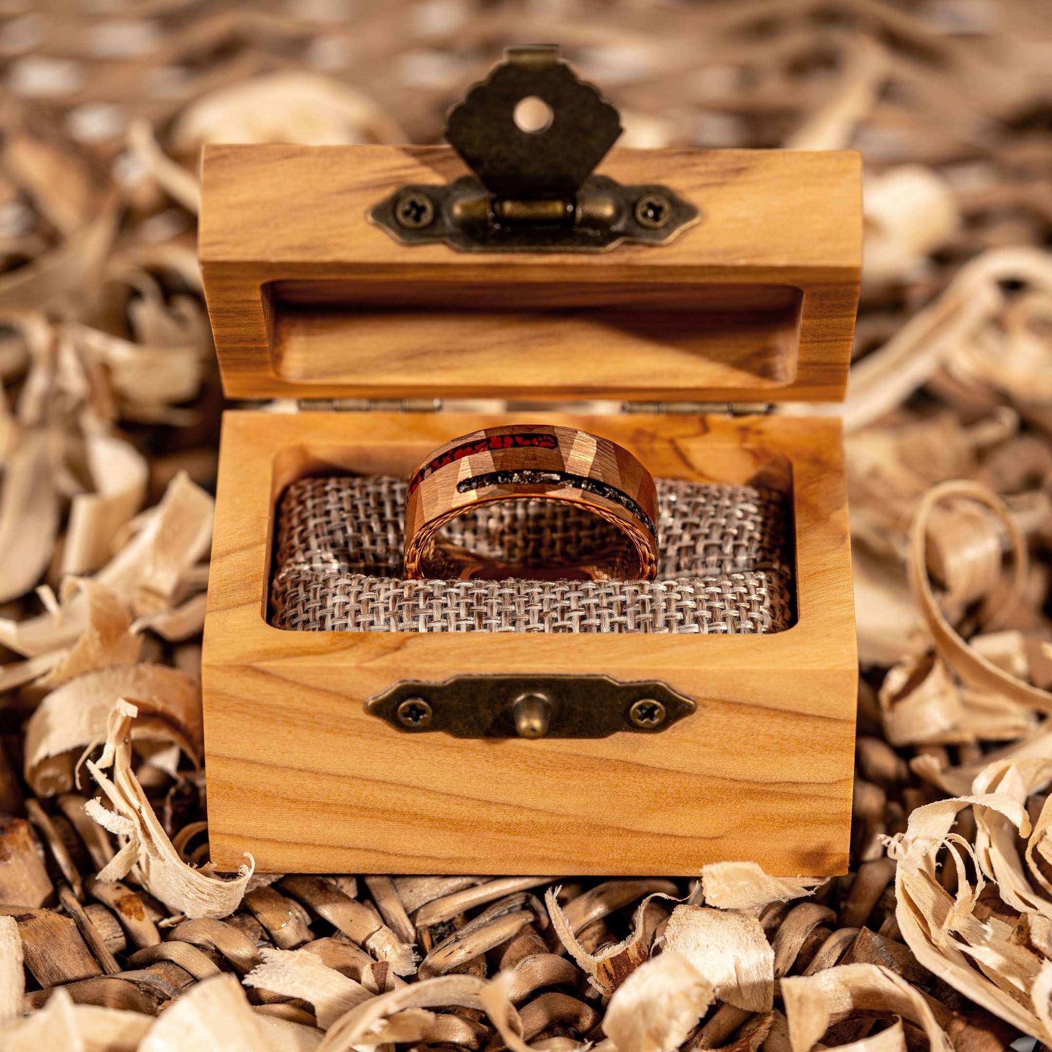 Dinosaur bone and meteorite ring displayed in a wooden box on decorative wood shavings.