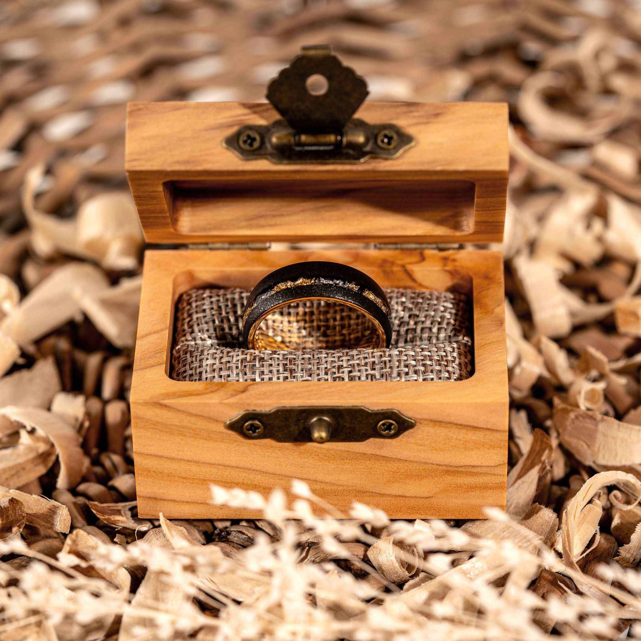 Sandblasted gold leaf meteorite ring in olive wood box on shredded wood background.