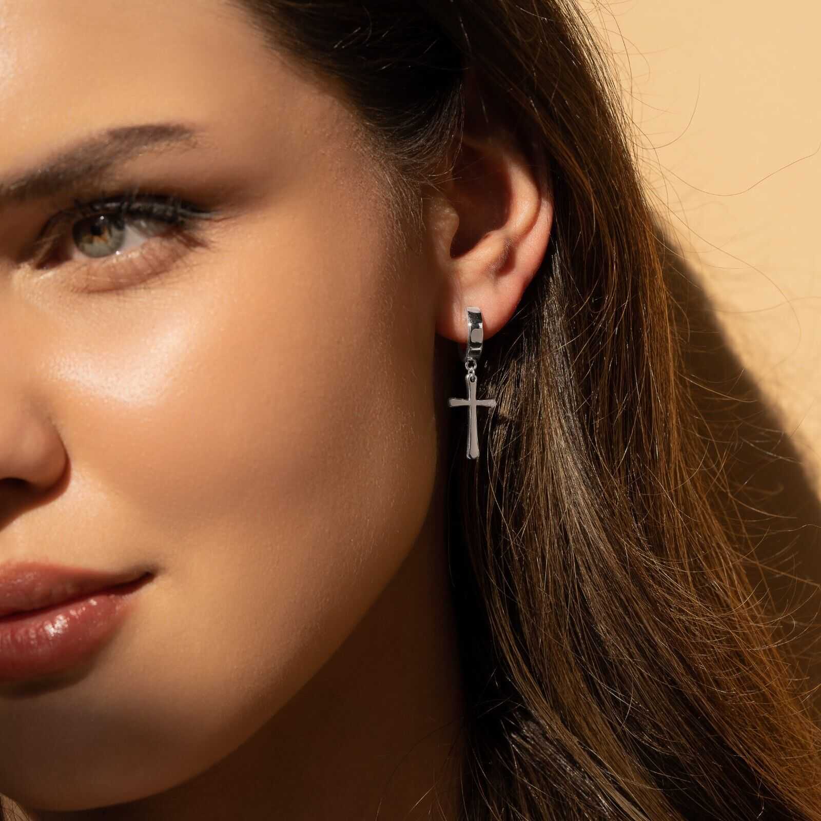 Sterling silver cross earrings with rhodium plating worn by a woman.