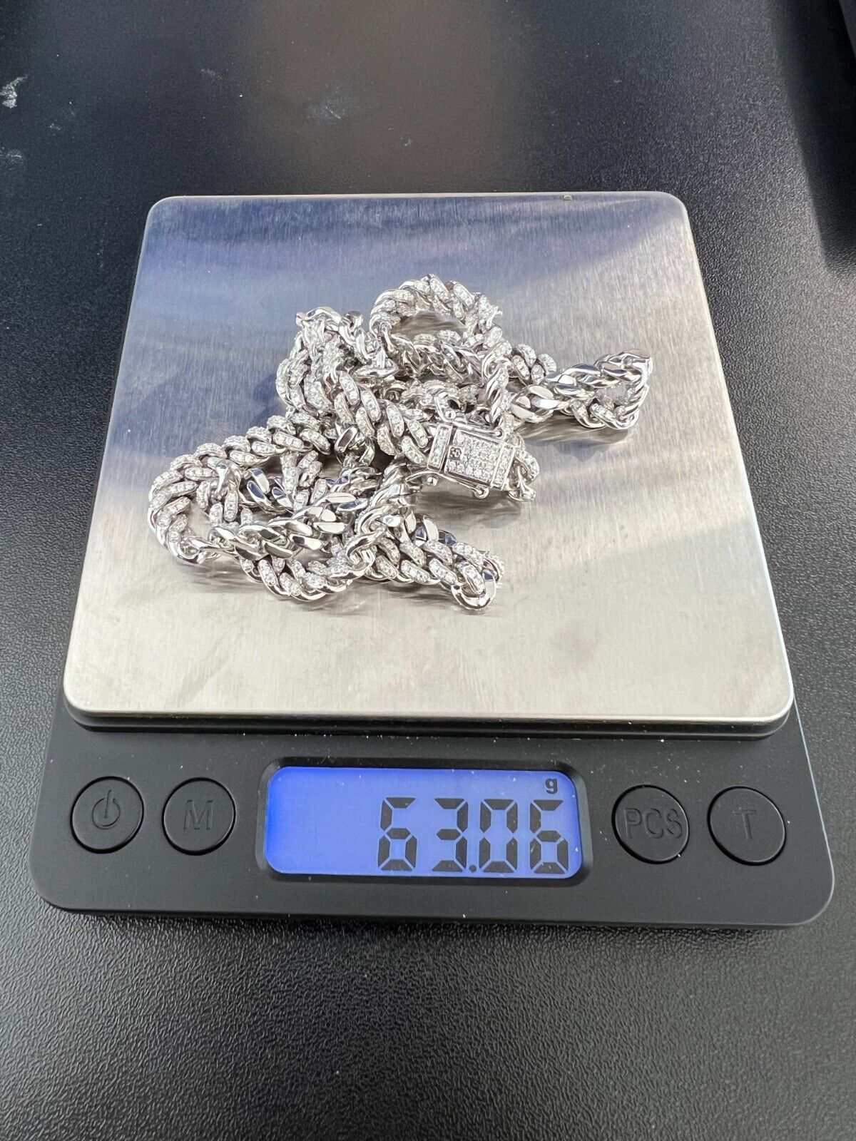 Men's moissanite Cuban curb link chain necklace on digital scale displaying 63.06 grams.