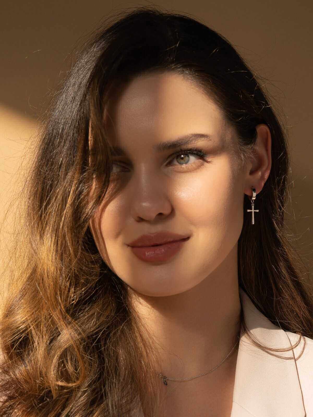 Sterling silver cross earrings with a hoop design worn by a woman, adding elegance and spirituality.