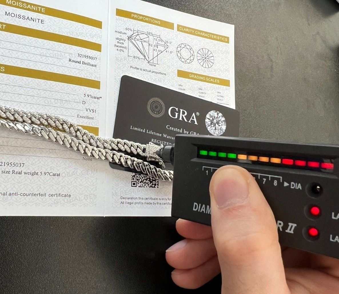 Men's iced moissanite Cuban curb link chain in 925 silver with diamond tester next to GRA certificate.
