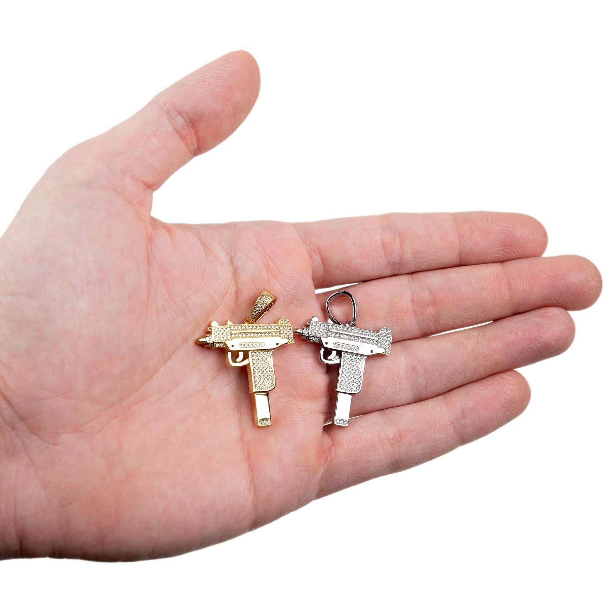Hand holding two Uzi pendants in gold and silver with clear CZ stones.