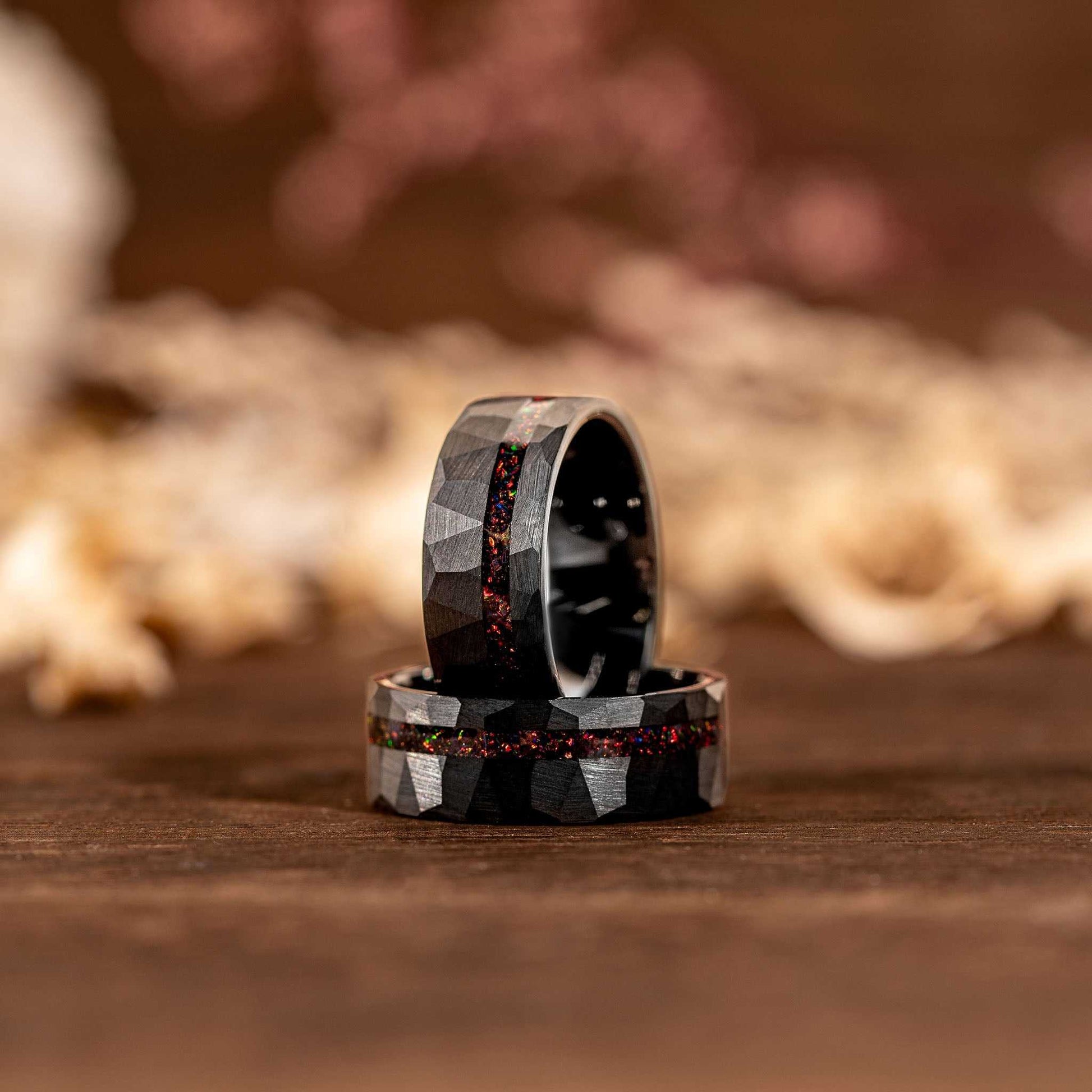 Black tungsten opal ring with hammered texture and iridescent inlay on a wooden surface