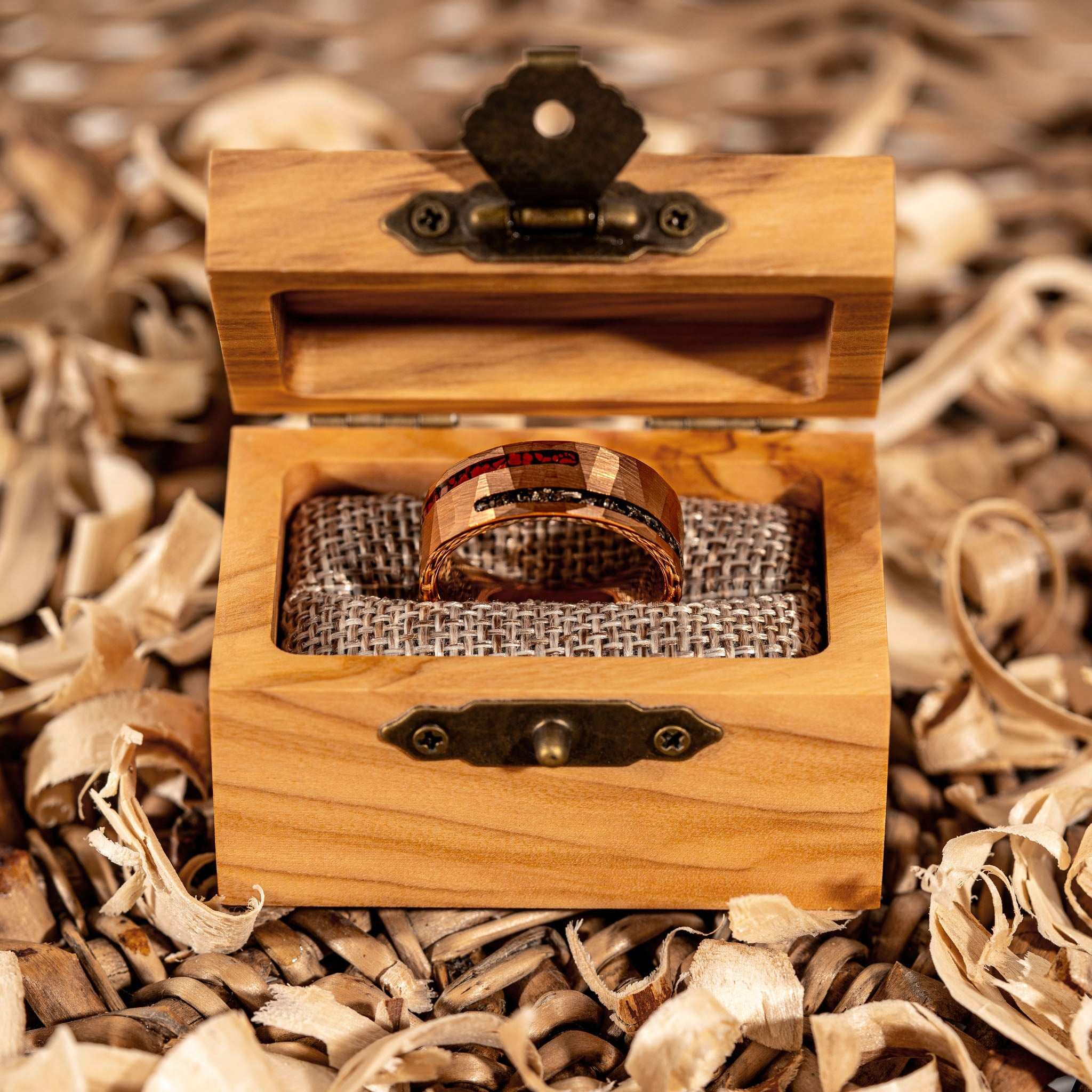 Dinosaur bone and meteorite ring displayed in a wooden box on decorative wood shavings.