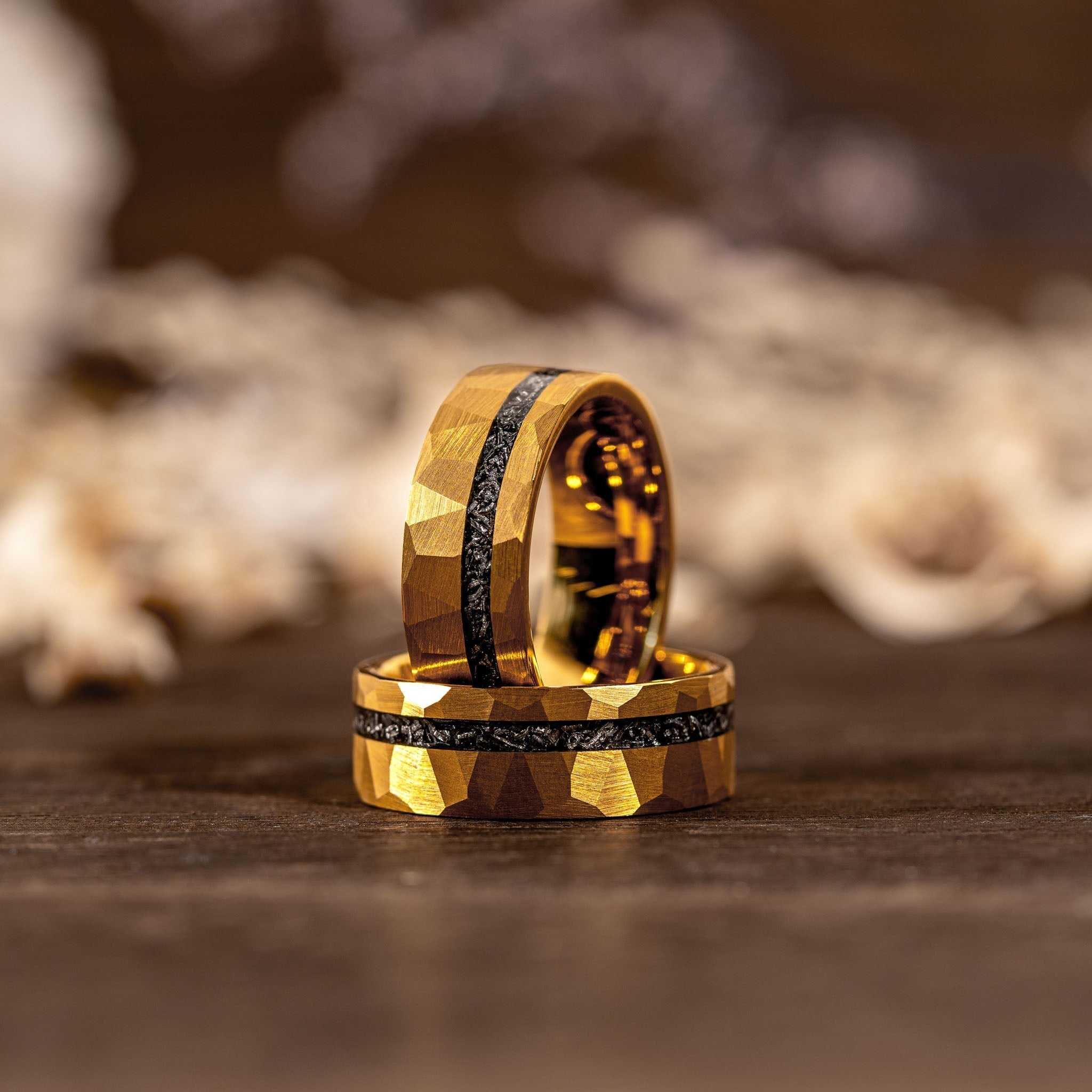 Two handcrafted 8mm tungsten carbide wedding rings with 18K yellow gold hammered finish and authentic meteorite inlay on wooden surface