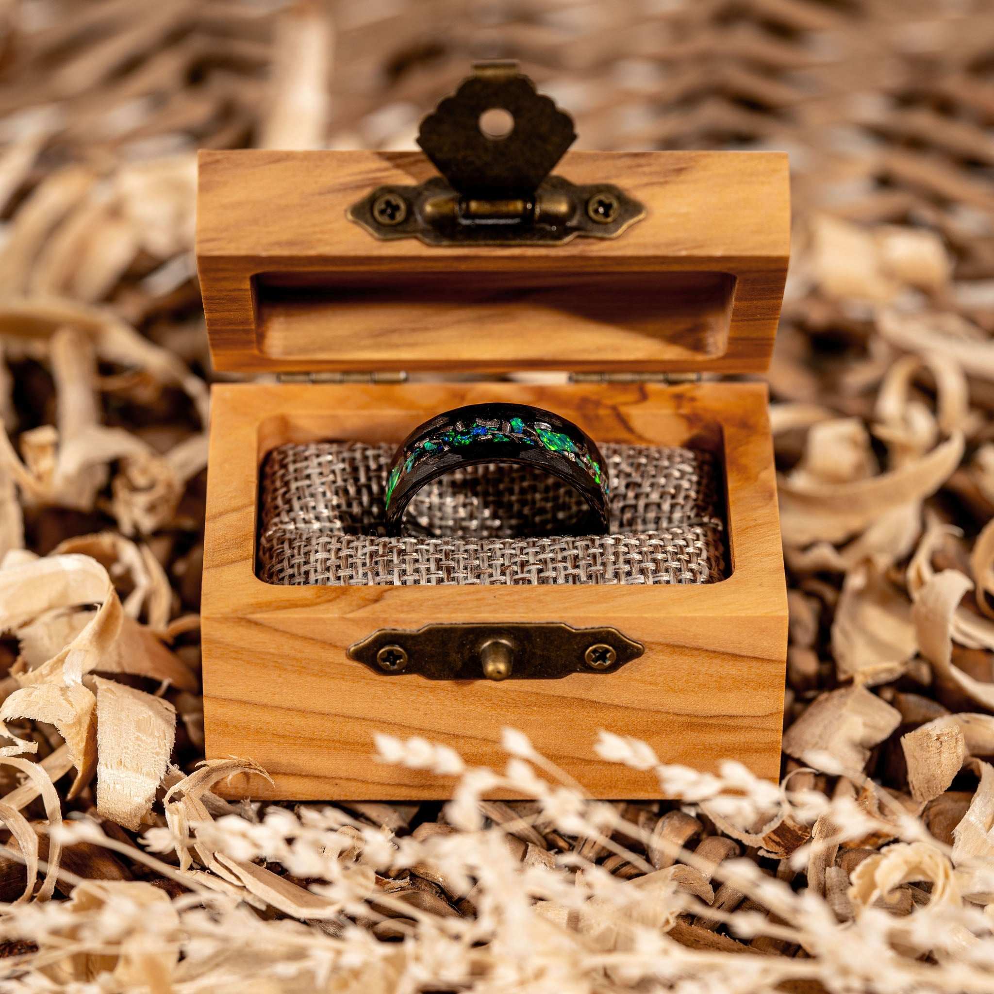 Meteorite and green opal ring in a wooden box surrounded by natural shavings.