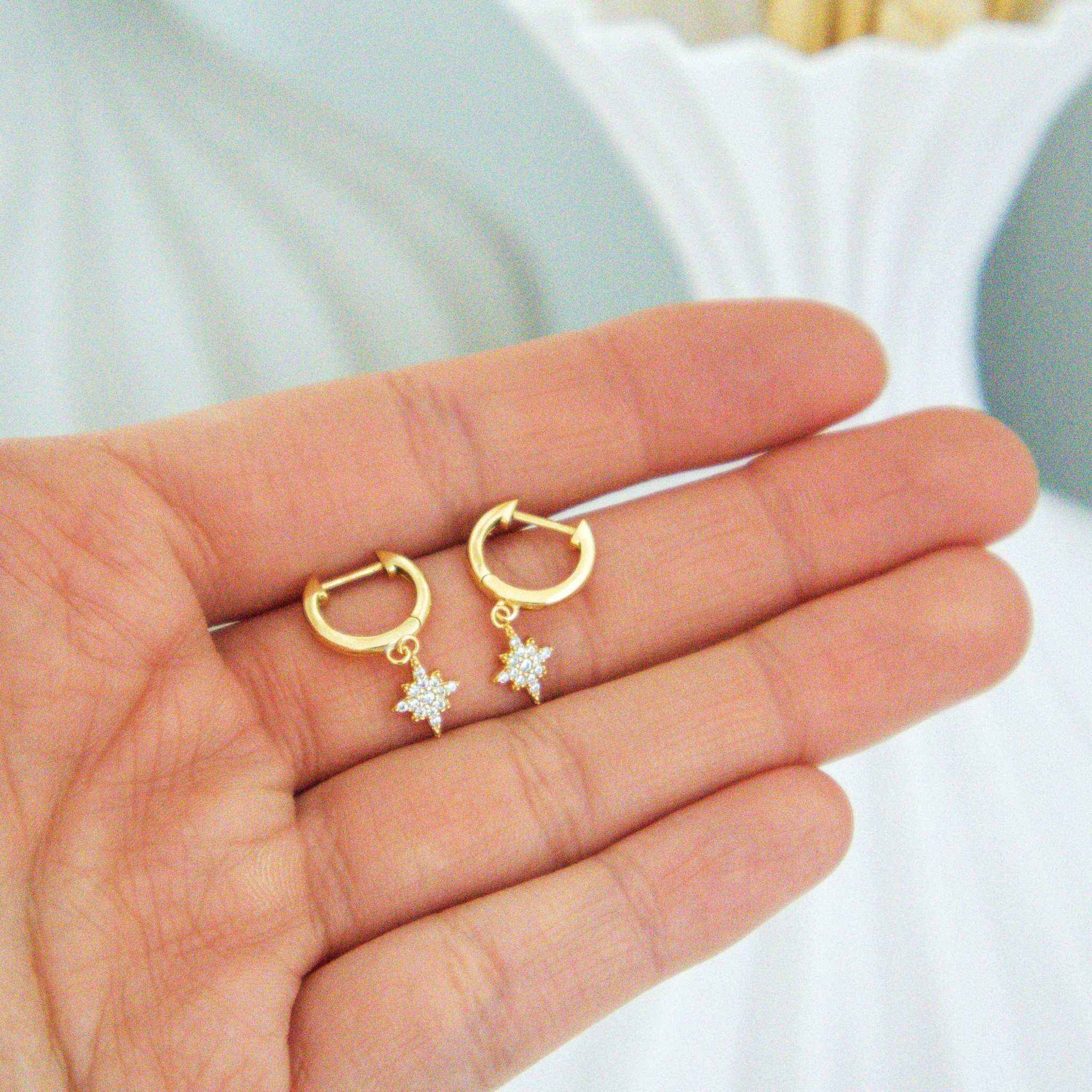 Stellar Starburst Earrings in 14K gold finish with CZ stones on open hand.